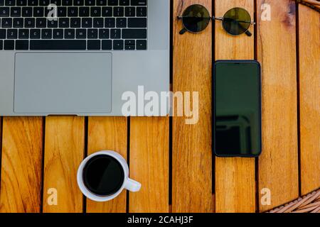 Arbeitsplatz minimalistisches Konzept mit grauem modernen Laptop und Smartphone zum Arbeiten auf natürlichem Holz braunen Schreibtisch. Zeit für eine Kaffeepause, eine Tasse schwarzen Coff Stockfoto