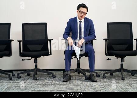 Junge männliche asiatische Arbeitssuchende im Stuhl sitzend scheint frustriert und besiegt zu sein Stockfoto