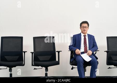 Ältere asiatische Arbeitssuchende Vorbereitung für Interview mit geschlossenen Augen während der Wartezeit in der Schlange Stockfoto