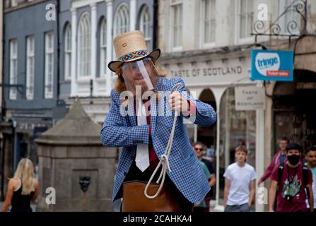 Royal Mile, Edinburgh, Schottland, Großbritannien. August 2020. 'Todd Various' Edinburgh Street Performer entscheidet, dass die Show weitergehen muss.das Fringe Festival 2020 wurde wegen der Covid-19 Pandemie abgesagt, aber heute wäre der Eröffnungstag des diesjährigen Fringe Events gewesen. Die Annullierung ist die erste seit ihrer Gründung im Jahr 1947. Todd trug ein schützendes Visier und führte Zaubertricks für ein sozial distanziertes kleines Publikum durch, denn das ist alles, was er tun darf. Während der Vorstellung musste er ständig Passanten bitten, weiter zu gehen, aber alle halbe Stunde zu seiner nächsten Show zurückzukehren. Stockfoto