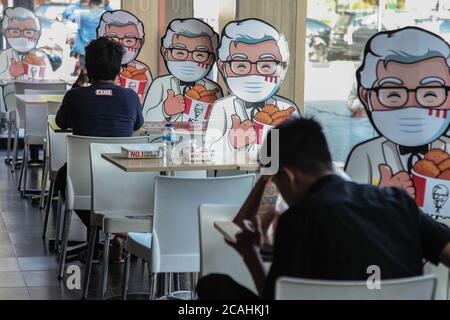 Medan, Nord-Sumatra, Indonesien. August 2020. Besucher sitzen in der Nähe von Colonel Sanders' Kartonausschnitt, der auf einem Stuhl montiert ist, um soziale Distanz in einem KFC-Restaurant in Medan, Nord-Sumatra, anzuwenden. Präsident Jokowi fragte seine Mitarbeiter, dass die Einhaltung von Gesundheitsprotokollen wie Händewaschen, Distanzhalten und das Tragen von Masken ein besonderes Anliegen sei, um die Ausbreitung des Coronavirus zu kontrollieren. Quelle: Albert Ivan Damanik/ZUMA Wire/Alamy Live News Stockfoto