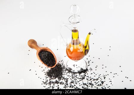 Schwarzes Kreuzkümmelöl mit Samen auf Holzgrund. Glasflasche mit schwarzen Kreuzkümmel Samen ätherisches Öl, Nigella Sativa in Löffel und Schüssel auf Holz rustikal b Stockfoto