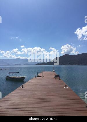 Vertikale Aufnahme eines hölzernen Dock am Meer umgeben Durch hohe felsige Berge Stockfoto