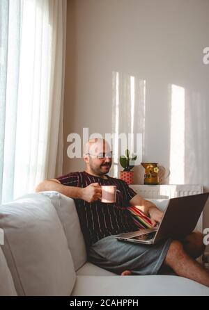 Junge Leute haben eine gute Zeit zu Hause. Musik hören, Kaffee und Tee trinken. Ruhender Teenager läuft mit Tablet und Leptop in den Händen. Stockfoto