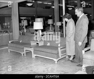 Circa 1940er Jahre, historisch, eine Dame in einem großen Möbel- und Innenraumgeschäft, die ein Paar Moern, kleine zwei-Sitzer-Sofas, mit passendem männlichen Kundenvertreter in Anwesenheit, USA, betrachtet. Stockfoto