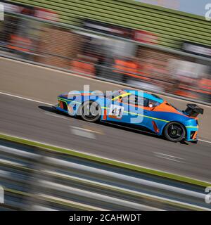 Eine Schwenkaufnahme eines blauen und orangenen Rennwagens, der eine Strecke fährt. Stockfoto