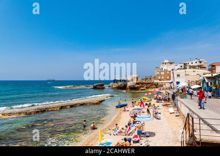 BATROUN, LIBANON - 02. Jun 2019: Touristen und Einheimische genießen den Strand von Batroun an der libanesischen Küste mit der berühmten phönizischen Mauer und Chez Magu Stockfoto