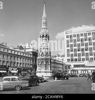 1960er Jahre, historisches Bild des Vorplatzes zum Bahnhof Charing Cross am Strand, London, zeigt Autos der Epoche und die viktorianische Nachbildung (1883) eines Eleanor Cross, Eines von mehreren ornmanentalen Kreuzen, die die Leiche der Königin Eleanor Ruhestätte auf ihrer Reise nach Westminster Abbey im Jahr 1290 markiert. Im Hintergrund sieht man das neu gebaute 'moderne' Villiers House. Stockfoto