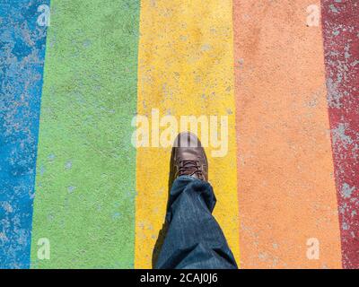 Draufsicht auf einen männlichen Fuß auf einem Regenbogen gefärbt Sidewalk – LGBT-Konzept Stockfoto