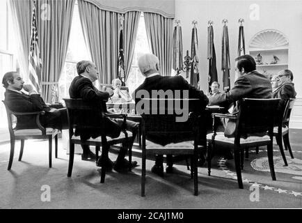 In diesem Aktenfoto wurden Extra Chairs am 9. Oktober 1974 in das Oval Office im Weißen Haus in Washington, DC gezogen, als sich die leitenden Berater des US-Präsidenten Gerald R. Ford um seinen Schreibtisch versammelten, um eines ihrer häufigen Treffen zu veranstalten. Gegen den Uhrzeigersinn von Präsident Ford sind diese Berater wie folgt: Ronald H. Nessen, Pressesprecher; John O. Marsh, Jr., Berater; Philip W. Buchen, Counsel; Donald Rumsfeld, Assistent; Paul Miltich, stellvertretender Pressesprecher; Brent Scowcroft, stellvertretender Assistent für nationale Sicherheitsangelegenheiten; und Robert Hartmann, Berater. Weltweite Nutzung Stockfoto