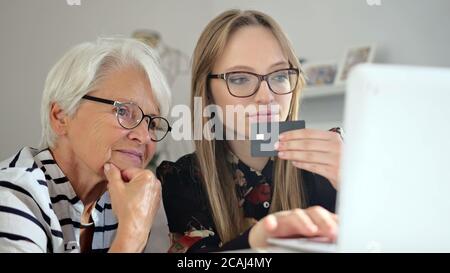 Enkelin hilft ihrer Großmutter, Online-Shopping zu tun. Bestellung von Waren online. Hochwertige 4k-Aufnahmen Stockfoto