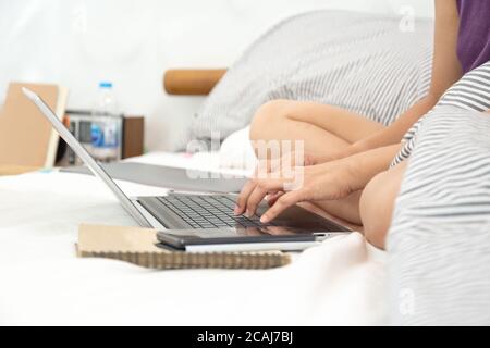 Frauen sitzen im Schlafzimmer auf dem Bett und arbeiten mit dem Computer. Stockfoto