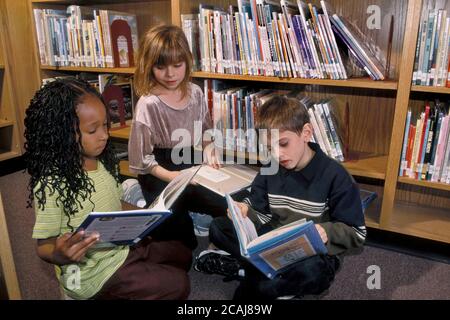 Austin, Texas USA: Ethnisch vielfältige Gruppe von Schülern im Kindergarten lesen Bilderbücher in der Schulbibliothek. HERR ©Bob Daemmrich Stockfoto