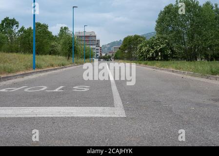 'Stop' geschrieben auf Asphaltstraße mit blauem Himmel, Wolken, Berge und Häuser im Hintergrund Stockfoto