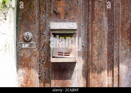 Ein alter, abgenutzter, verrostet und unbeschrifteter Briefkasten, montiert auf einer alten verwitterten Holztür. Daneben ist eine unbeschriftete Glocke. Stockfoto