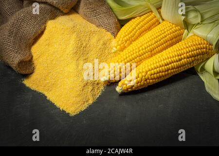 Reife junge süße Maiskolben, auf der linken Stapel Maismehl auf dunklem Hintergrund, kopieren space.Gluten frei Lebensmittelkonzept Stockfoto