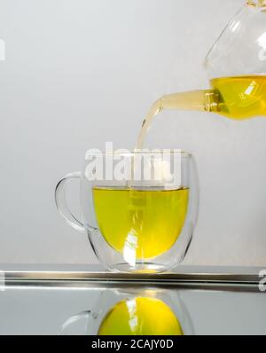 Teekanne aus Glas gießen grüner Tee in den Becher isoliert auf weißem Stockfoto
