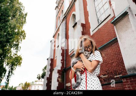 Junge blonde Mädchen hält in ihren Armen und umarmt liebevoll Ihr Haustier Hauskätzchen Rasse Scottish Straight in der Stadt Stockfoto