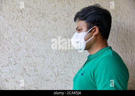 Erwachsene mittleren Alters gut gebaut Mann trägt N95 Maske geben Profil Schuss gegen eine beige strukturierte Wand mit negativem Raum für Text Stockfoto