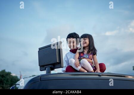 Junge und Mädchen tun Hausaufgaben mit Computer auf dem Dach des Autos, New Normal Bildung Konzept Stockfoto