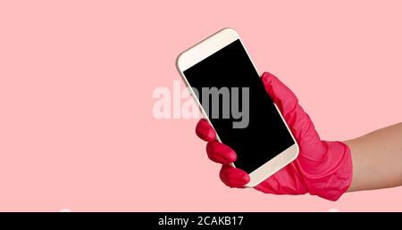 Hand in Handschuhe halten Smartphone mit mockup auf rosa Hintergrund. Kontaktloser Einkauf und Lieferung. Stockfoto