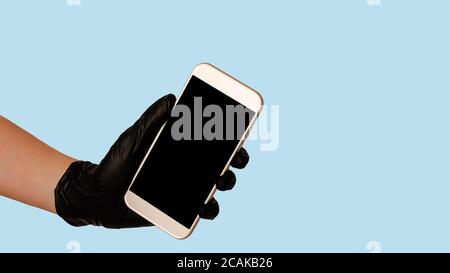 Hand in schwarzem Handschuh hält Smartphone mit leerem leeren Bildschirm auf blauem Hintergrund. Konzept der sicheren Lebensmittelzustellung. Stockfoto