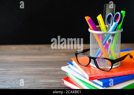 Zurück zur Schule. Stapel von Büchern, Schulbedarf und Brille auf schwarzem Brett Hintergrund. Bildungskonzept. Stockfoto