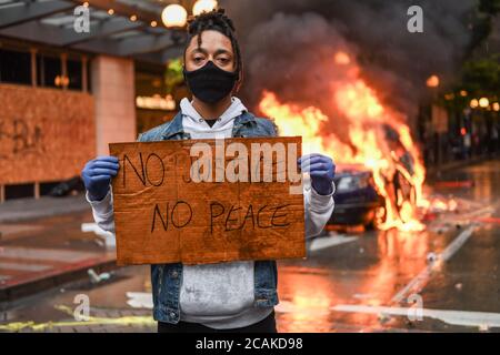 Seattle, USA, 30. Mai 2020: Ein Aktivist hält ein Zeichen NO JUSTICE NO PEACE, während ein Polizeiauto in Westlake im Hintergrund brennt. Stockfoto