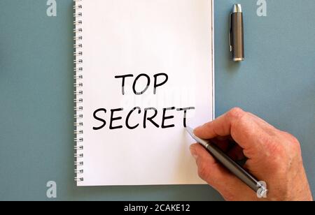 Männliche Hand schreiben "top secret" auf weißer Note, isoliert auf blauem Hintergrund. Stockfoto