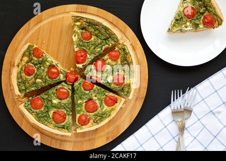 Hausgemachter Spinat Quiche auf einem runden Bambusbrett auf schwarzem Hintergrund, Draufsicht. Flachlage, über Kopf, von oben. Stockfoto