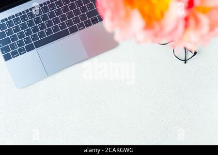 Arbeitsplatz, Desktop-Ansicht. Laptop, pinkfarbenes Pfingstrosen, Brille im Modell. Arbeitsplatz für Frauen. Speicherplatz kopieren. Stockfoto