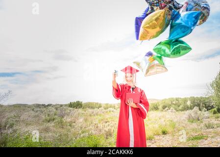 Junge Frau feiert Abitur, hält Ballons und Diplom. Stockfoto