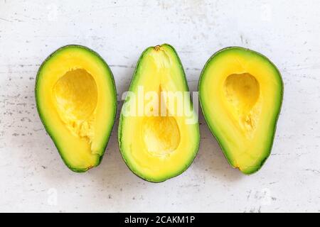 Drei reife Avocado Hälften mit hellgelbem Fruchtfleisch auf weißem Arbeitsbrett, Tischplattenansicht Stockfoto