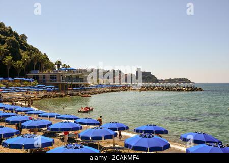 Panoramablick auf die Bucht mit Reihen von Sonnenschirmen am Sandstrand und das alte Fischerdorf Lerici im Hintergrund im Sommer, Ligurien, Italien Stockfoto