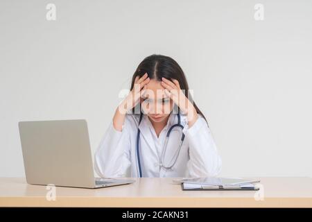 Junge asiatische Frau Arzt auf dem Schreibtisch sitzen, sie unglücklich und müde aussehen wegen Überlastung, Konzept der gestressten erschöpft und Arzt Haftung, Umgang Stockfoto