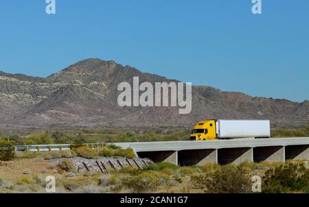 Großer Langstrecken-Sattelschlepper mit zwei flachen Betten Sattelauflieger transportieren auf der kurvenreichen Straße mit Brücke herum Der Bergfelsen in den USA Stockfoto