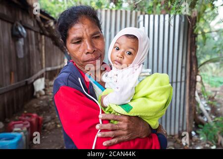 Haikesa / Indonesien - 10. August 2018: Timoresische ältere Frau mit niedlichem Baby und großen Augen in den Armen Stockfoto