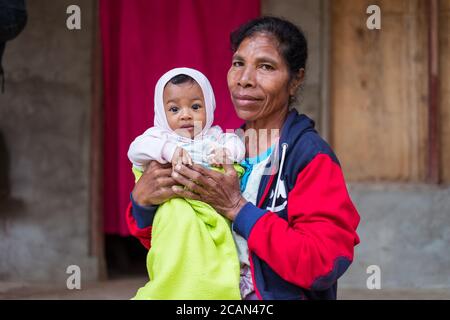 Haikesa / Indonesien - 10. August 2018: Timoresische ältere Frau mit niedlichem Baby und großen Augen in den Armen Stockfoto