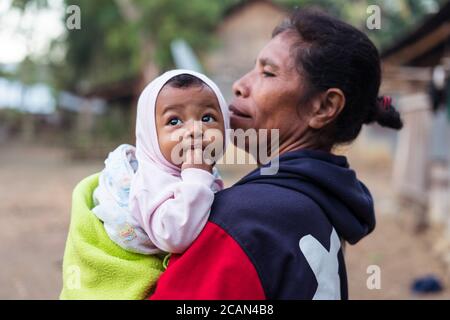 Haikesa / Indonesien - 10. August 2018: Timoresische ältere Frau mit niedlichem Baby und großen Augen in den Armen Stockfoto