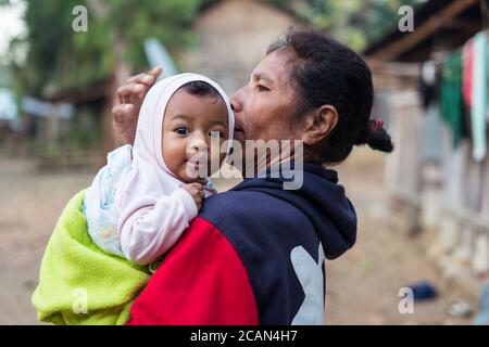 Haikesa / Indonesien - 10. August 2018: Timoresische ältere Frau mit niedlichem Baby und großen Augen in den Armen Stockfoto