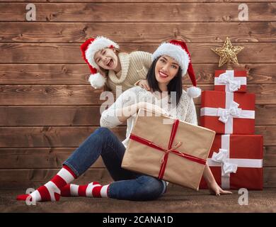 Frohe Weihnachten und Happy Holidays Konzept. Mutter und Kind Mädchen mit weihnachtsgeschenken auf Holzhintergrund. Porträt einer schönen Familie in Santa Stockfoto