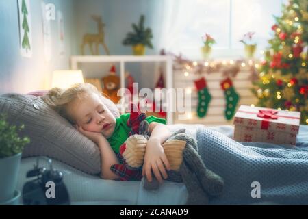 Frohe Weihnachten und frohe Feiertage! Nettes kleines Kind Mädchen schlafen im Bett in der Nähe von Baum zu Hause. Stockfoto