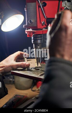 Hände eines Mannes, der in einer Hauswerkstatt ein Metallteil auf einer Werkzeugmaschine bohrt. Stockfoto