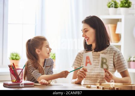 Frohe Familie. Mutter und Tochter lernen zu schreiben. Erwachsene Frau lehrt Kind das Alphabet. Stockfoto