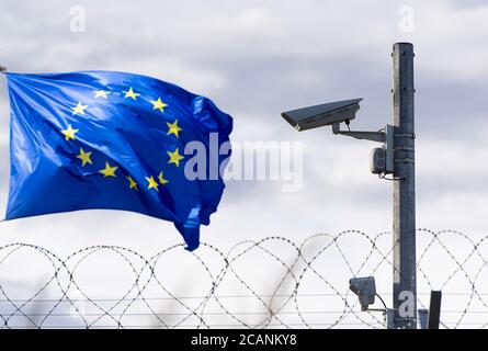 EU-Flagge und EU-Grenze mit Überwachungskamera und Stacheldraht, Konzeptbild Stockfoto