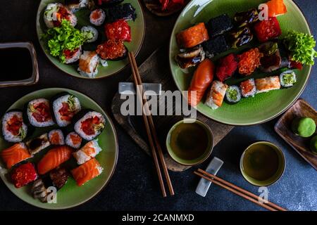 Sushi-Set mit verschiedenen Sashimi, Sushi-Brötchen und Tee auf Steinschiefer Stockfoto