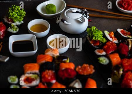 Sushi-Set mit verschiedenen Sashimi, Sushi-Brötchen und Tee auf Steinschiefer Stockfoto