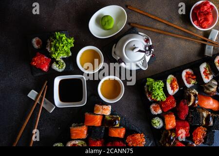 Sushi-Set mit verschiedenen Sashimi, Sushi-Brötchen und Tee auf Steinschiefer Stockfoto