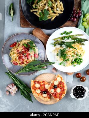 Auswahl an hausgemachten veganen Pasta, Pizza und Snacks auf grauem Hintergrund. Italienische Küche. Draufsicht, flach liegend Stockfoto