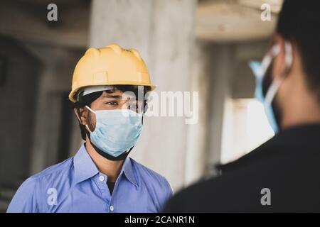 Zwei Bauarbeiter oder Ingenieure vor Ort sprechen durch das Tragen von medizinischen Gesichtsmaske bei gleichzeitiger Wahrung der sozialen Distanz - Konzept der Wirtschaft, Industrie Stockfoto